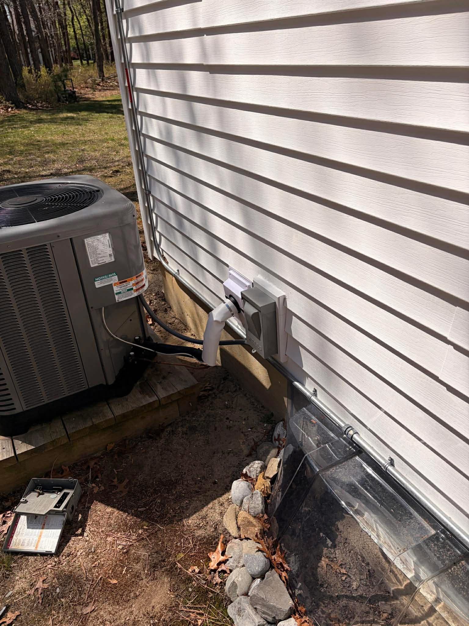 Outdoor air conditioning unit attached to a house exterior with visible pipes.