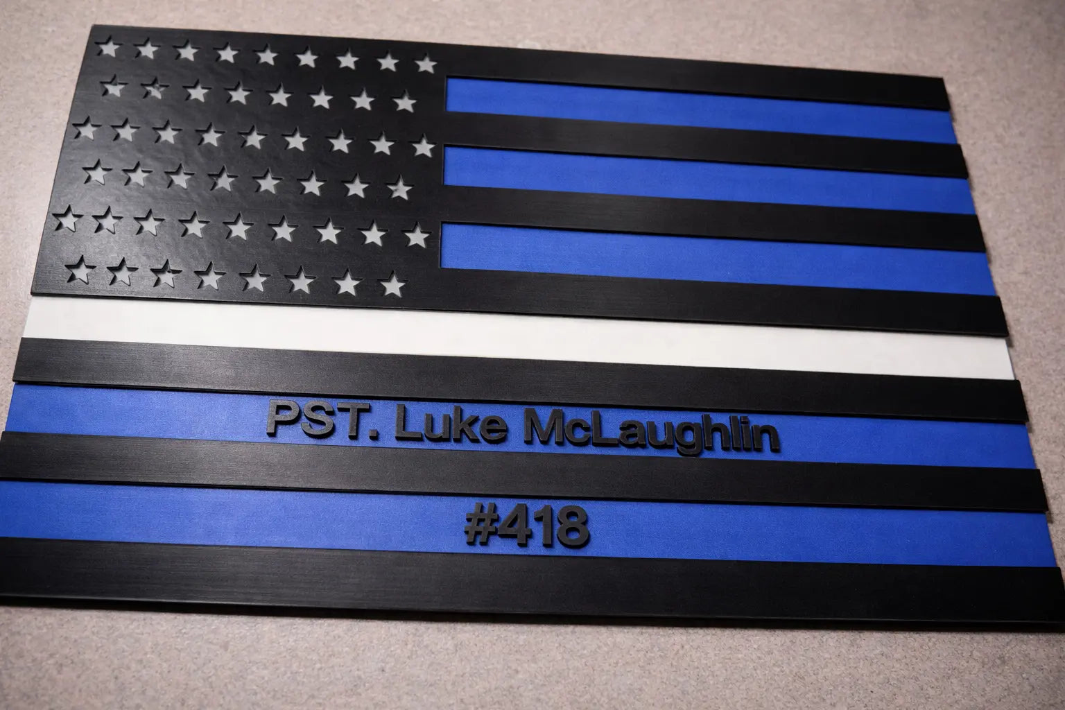 American flag with blue stripe and text 'PST. Luke McLaughlin #418' on a gray surface